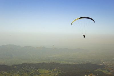 Person paragliding over mountains against clear sky