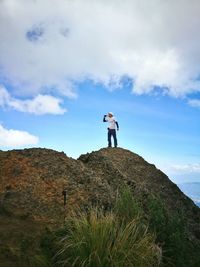 Low angle view of man drinking while standing on mountain against cloudy sky