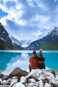 Rear view of men sitting by lake against mountains