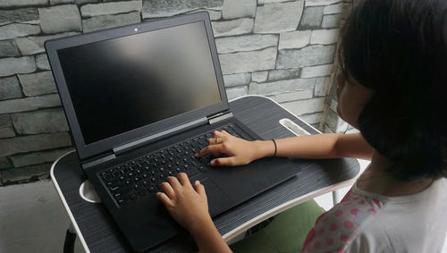 Cute asian little girl using the internet on a laptop computer to do her homework at home