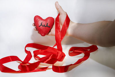 Close-up of hand holding red heart shape over white background