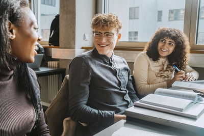 Cheerful multiracial friends talking while sitting in classroom in community college