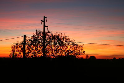 Silhouette trees and electricity pylon against sky during sunset