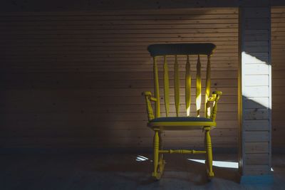 Sunlight falling on empty yellow rocking chair by wooden wall