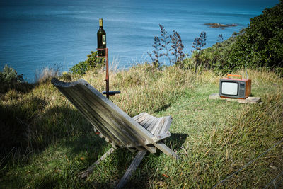 Empty chair on field by sea against sky