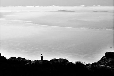 Distant view of silhouette person meditating on mountain