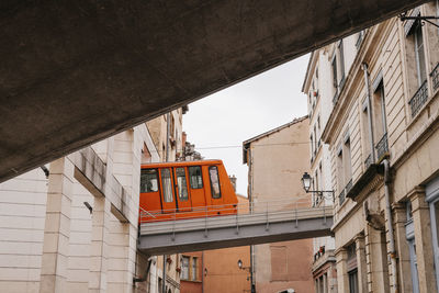 Low angle view of cable car moving on bridge amidst buildings in city