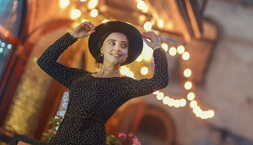 Young woman standing against illuminated string lights