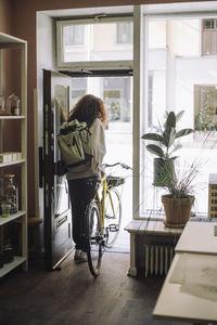 Rear view full length of female architect leaving with bicycle from office