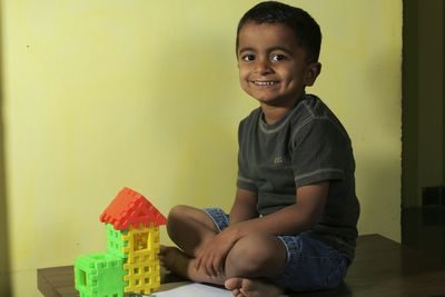 Portrait of happy boy playing with toy blocks on table by yellow wall