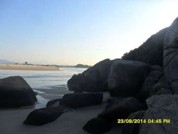 Rocks on beach against clear sky during sunset