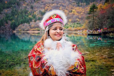 Smiling woman wearing traditional clothing standing against lake