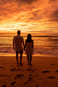 Rear view of women on beach against sky during sunset