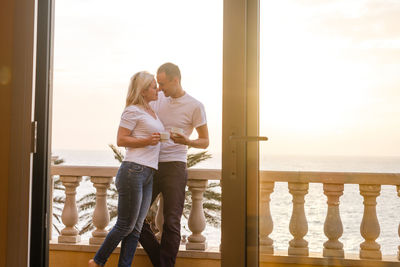 Happy couple with coffee cup standing in balcony