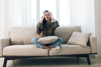 Young woman using phone while sitting on sofa at home