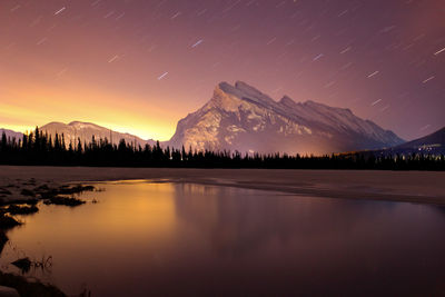 Scenic view of lake and mountains against star trail at night
