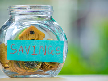 Close-up of coins and model house in glass jar on table