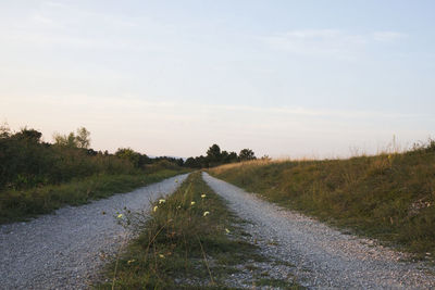 Empty road amidst field against sky