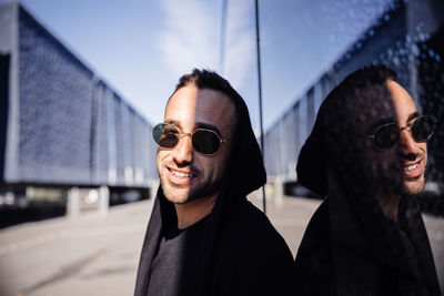 Man wearing sunglasses while leaning against glass wall