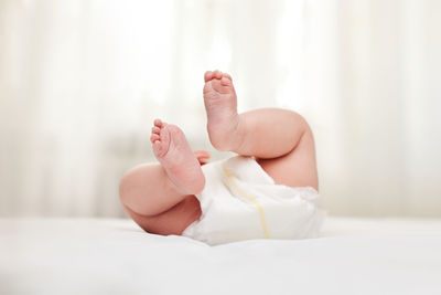 Low section of naked woman lying on bed at home