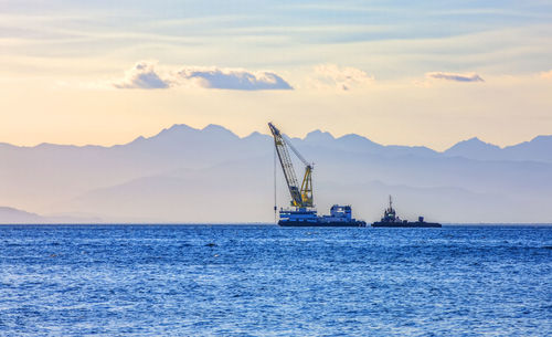 Sea ship with a crane on the background of a mountain range in the haze