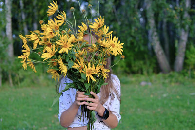 Girl hiding behind a bouquet of topinambur flowers. yellow flowers. summer country concept. 