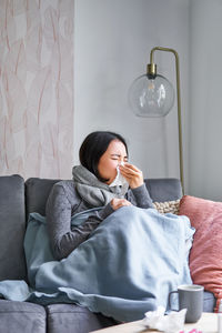 Portrait of young woman applying face on sofa at home