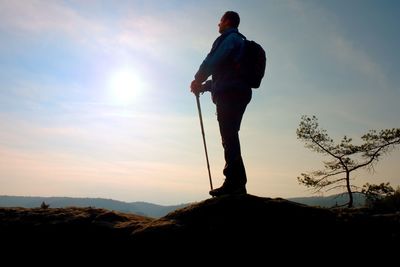 Tourist in windcheater with sporty trecking poles in hands stand on rocky view point