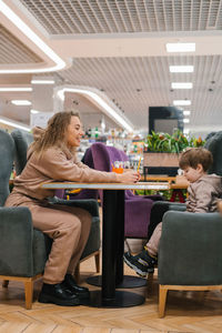 Young caucasian mother is sitting at a table in a cafe with her four-year-old son waiting 