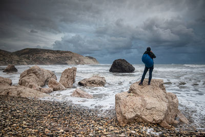 Rear view of man standing on rock at beach against sky