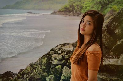 Portrait of young woman standing on rock by sea.