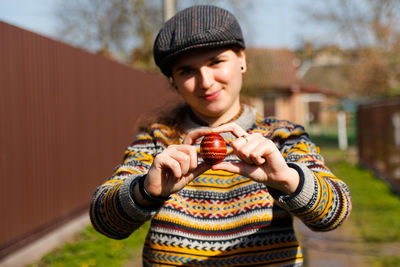 Happy smiling woman holding one colored red egg, easter holiday concept. hands holding modern