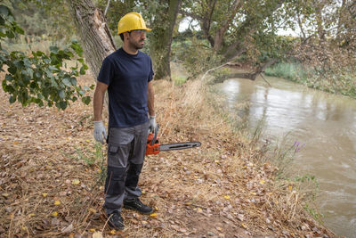 Full length of man holding chain saw standing in forest