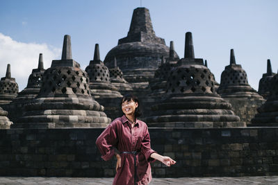 Smiling woman looking away while standing against temple and sky