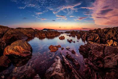 Scenic view of rock formations by sea against sky during sunset