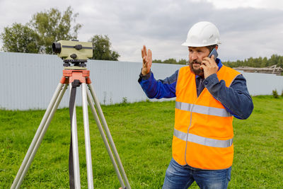 A disgruntled civil engineer with an optical level gauge speaks on a cell phone and swears. 