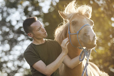 Portrait of man calming horse during obedience training on sunny summer day.