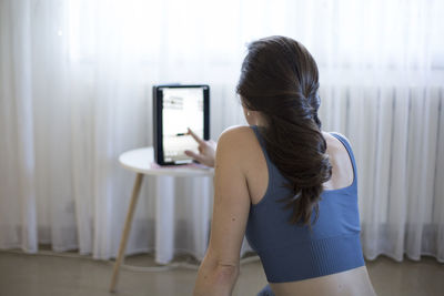 Rear view of woman using mobile phone at home