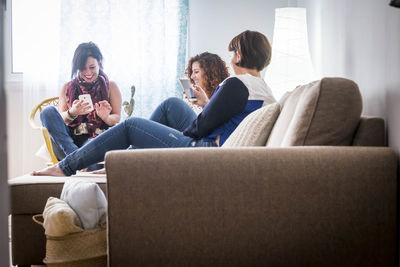 Friends using mobile phone while sitting on sofa at home