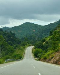 Road amidst trees and mountains against sky