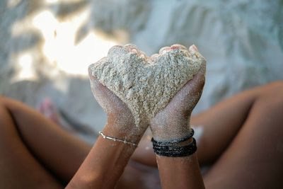 Midsection of woman holding sand in heart shape at beach