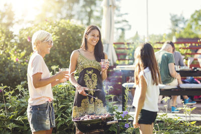 Happy women preparing food on barbecue while looking at girl in back yard