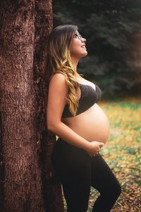 Midsection of woman standing by tree trunk