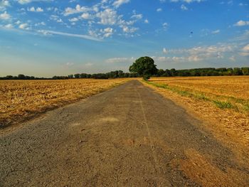 Dirt road amidst field against sky