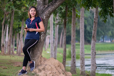 Full length of man using phone while sitting on tree