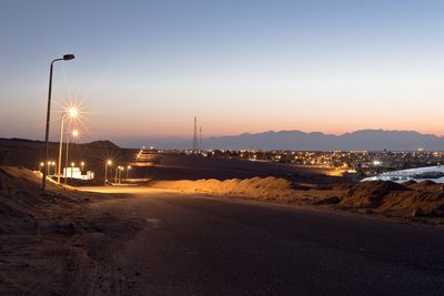 Street amidst illuminated city against sky during sunset