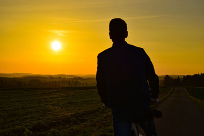 Silhouette man standing on field against sky during sunset