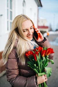 Girl at the train station is talking on a smartphone, a bouquet of tulip flowers in her hands
