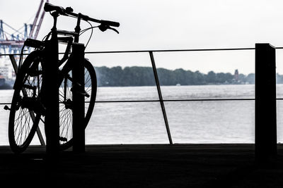 Silhouette bicycle by sea against clear sky