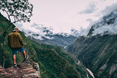 Rear view of man standing on mountain against sky